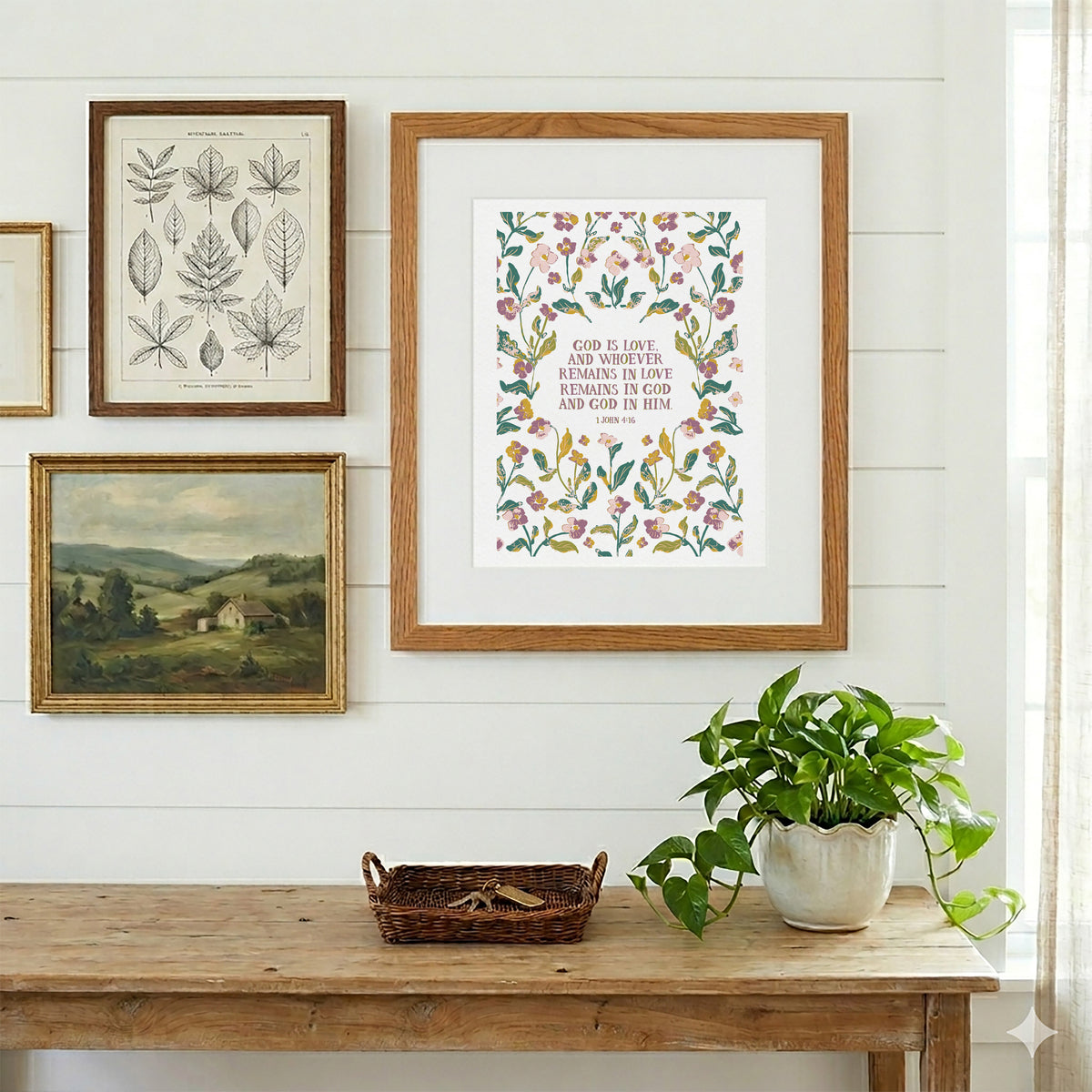 A framed botanical art print with a floral border and inspirational text hangs on a white shiplap wall above a rustic wooden table with a potted green plant and a small basket.