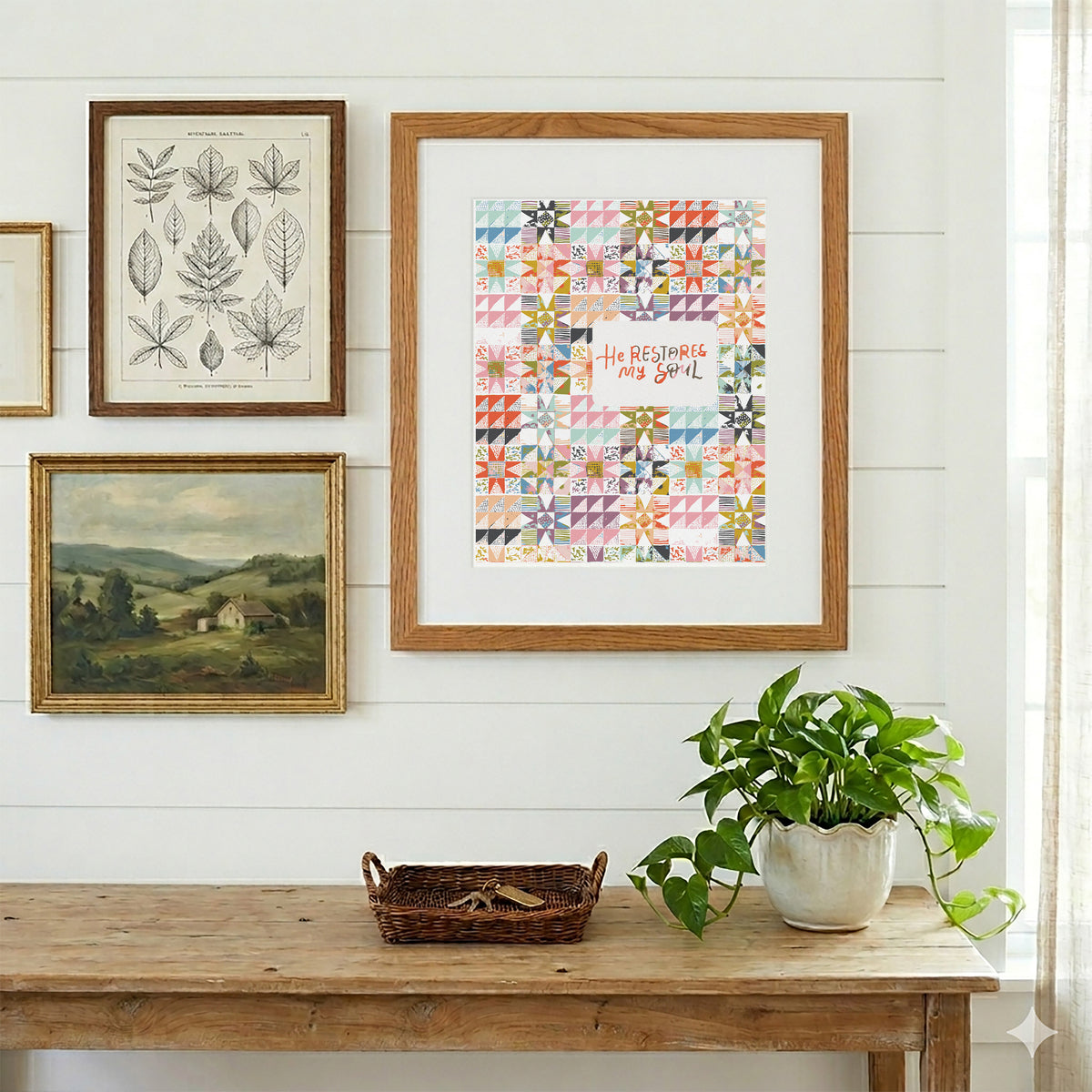 A framed art print featuring a colorful quilt pattern with the text 'He Respects My You!' hangs on a white shiplap wall above a rustic wooden console table with a potted green plant.