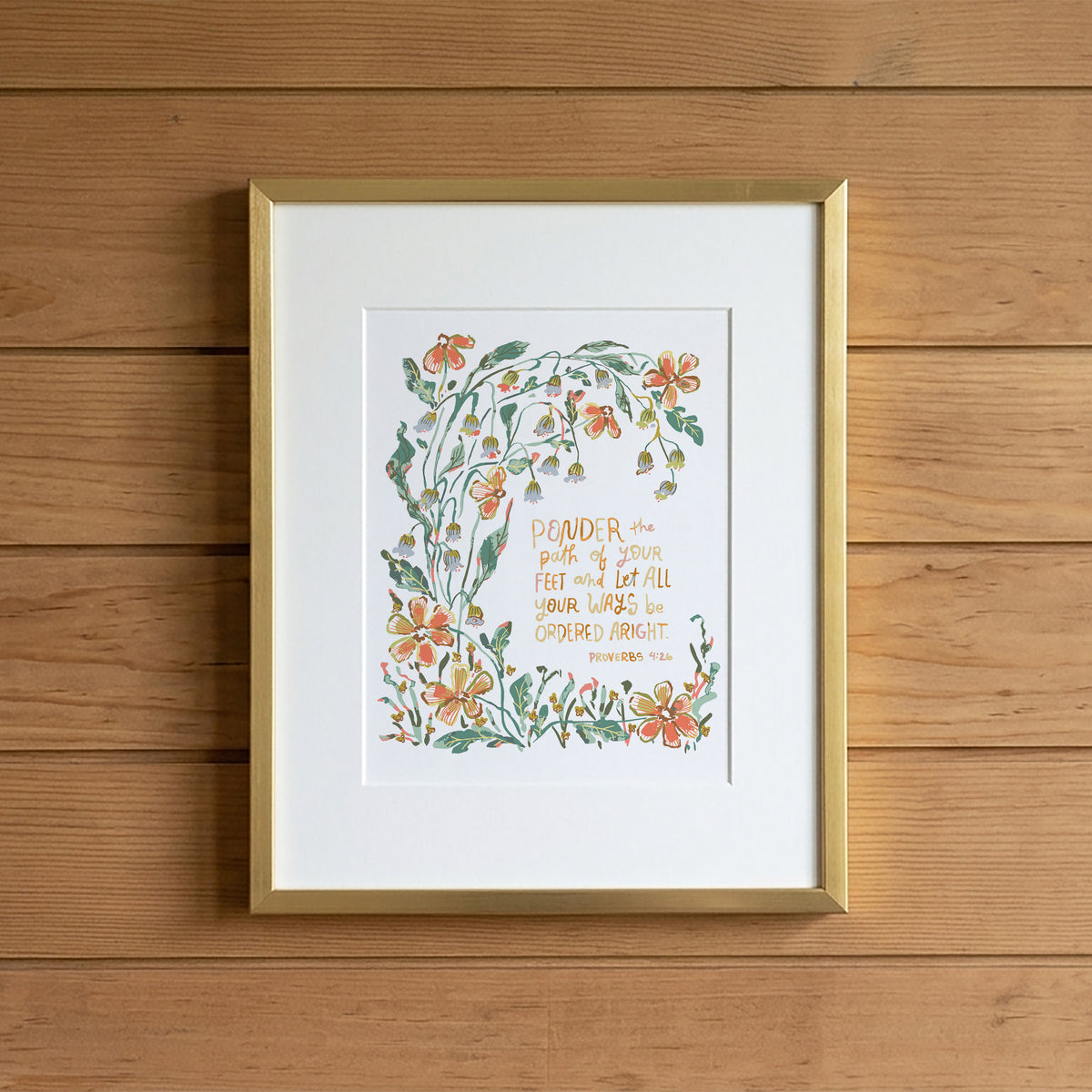 A framed art print featuring a botanical illustration with orange flowers and green leaves surrounding a handwritten quote, displayed on a light wood plank wall.