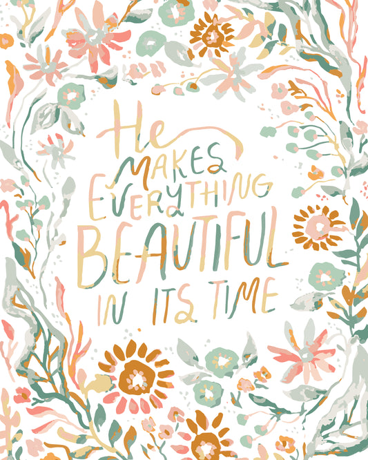A square art print featuring a hand-lettered quote that reads 'He makes everything beautiful in its time' in soft peach, sage green, and mustard tones, surrounded by a watercolor-style floral border on a white background.